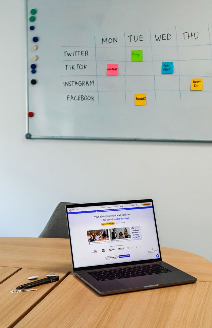 Un aménagement de bureau moderne avec un ordinateur portable et un planning sur tableau blanc pour les plateformes de réseaux sociaux.